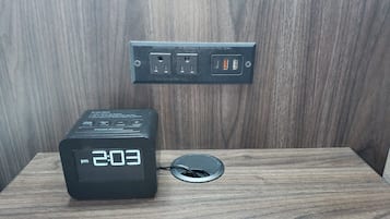 Um relógio digital mostrando 14:03 sobre uma mesa de madeira com uma régua de energia acima.
