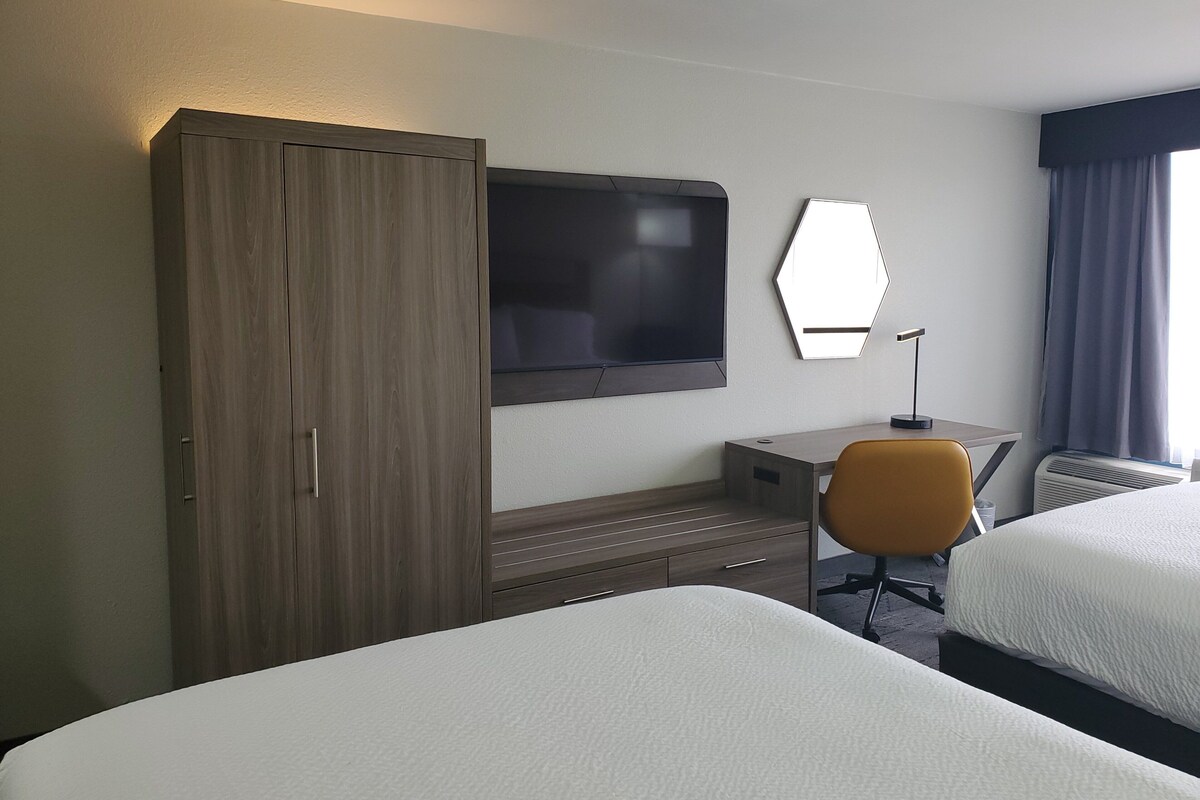 Quarto de hotel com duas camas, televisão, secretária, cadeira e guarda-roupa.