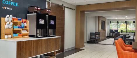 A modern coffee station with a sign that reads "MUST HAVE COFFEE." There are coffee machines, a refrigerator, and a counter with various coffee-related items. The area has a clean, contemporary design with a tiled floor and wooden accents.