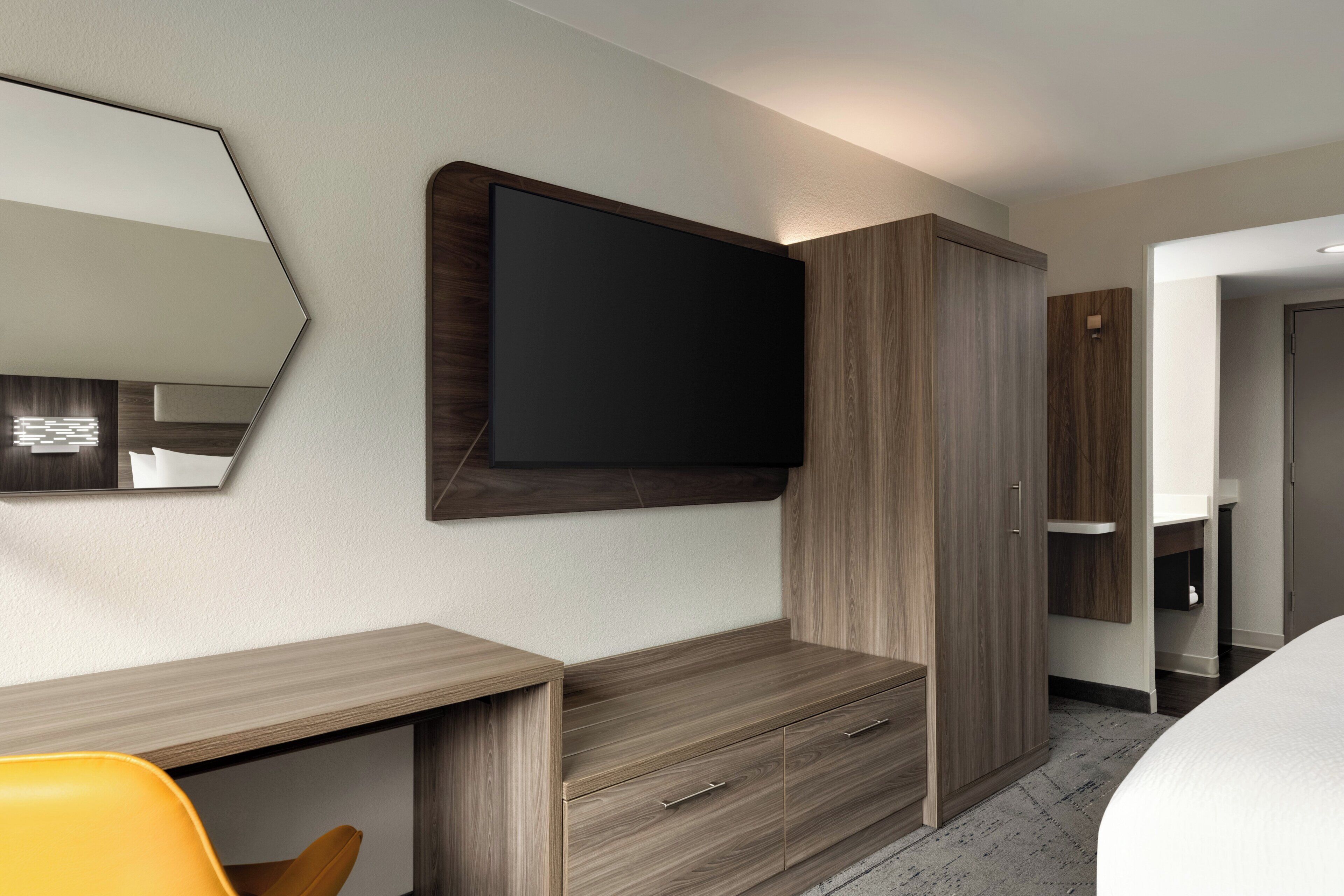 Une chambre d’hôtel moderne dotée d’un téléviseur à écran plat fixé au mur, de meubles en bois et d’un bureau avec une chaise.
