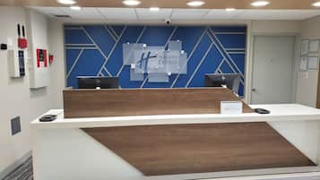 Mostrador de recepción de Holiday Inn Express con dos computadoras HP, una cámara de seguridad y una puerta a la derecha.