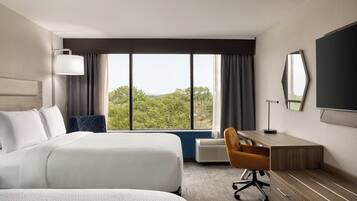 A hotel room with a large bed, a desk, a chair, a TV, and a window with a view of trees.