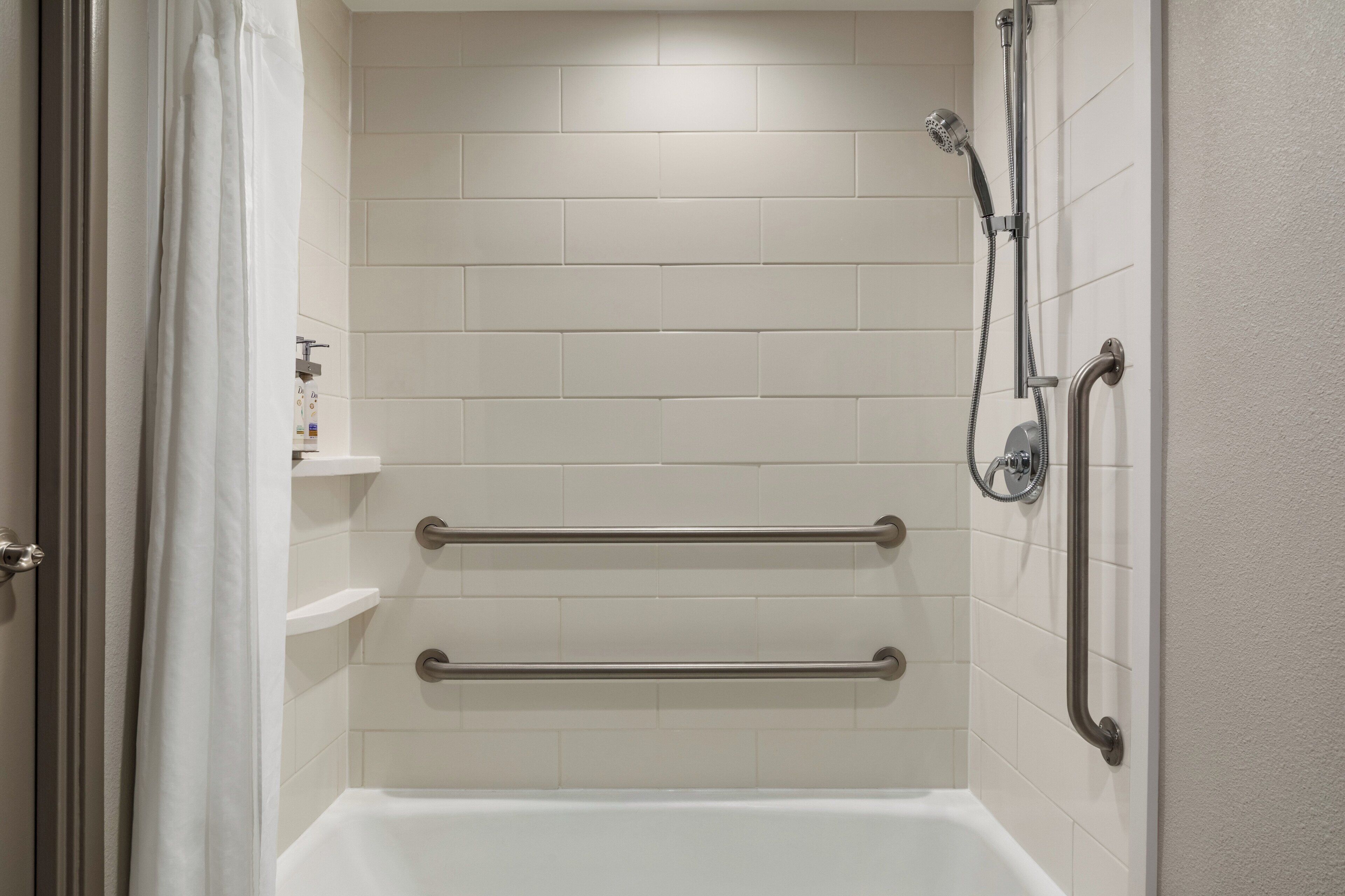A bathroom with a white bathtub, a showerhead, and grab bars.
