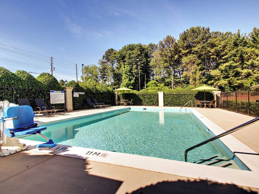Ein rechteckiger Pool mit klarem, blauem Wasser, umgeben von einem Metallzaun, ausgestattet mit Liegestühlen und Sonnenschirmen.