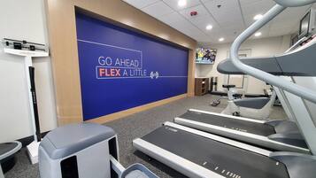 Un gimnasio con cintas de correr, una pared con texto motivacional y una pantalla de televisión.