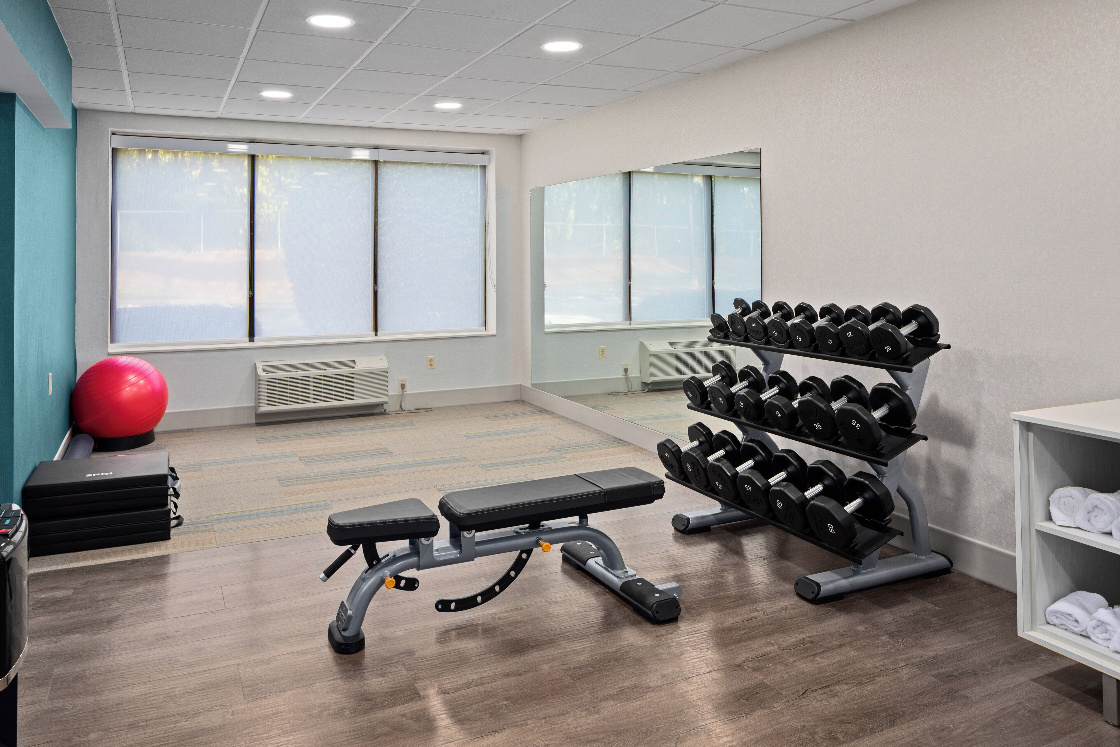 A gym with exercise equipment, a bench, a red exercise ball, and a rack of dumbbells.