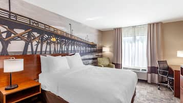 Een hotelkamer met een bed, een bureau, een stoel, een lamp en een muurschildering van een pier.