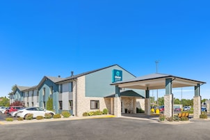 Un hotel con estacionamiento techado, un letrero que indica que es un establecimiento Clarion Pointe de Choice Hotels, y un cielo azul despejado.