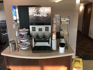 A coffee station with a coffee machine, bowls of sugar, and a caution sign.