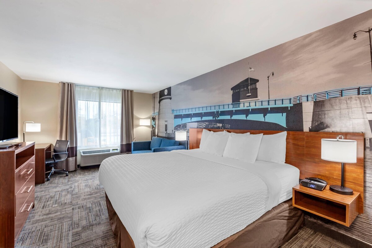 A hotel room with a large bed, a desk with a chair, a TV, and a painting of a bridge on the wall.