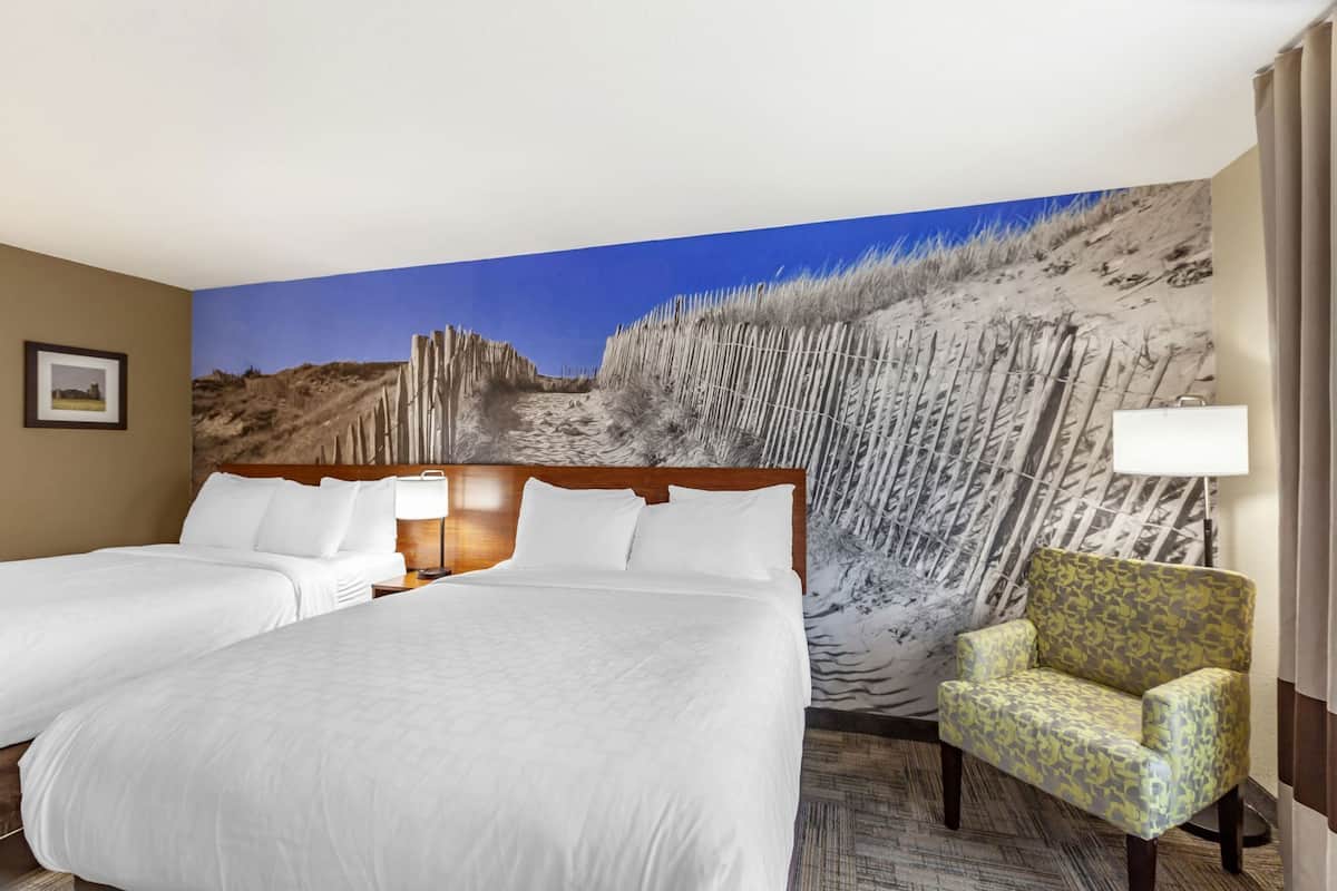 Ein Hotelzimmer mit einem großen Bett, zwei Nachttischen, einem Sessel und einem Wandbild einer Wüstenlandschaft.