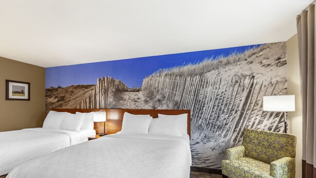 A hotel room with two beds, a large mural of a beach, a patterned armchair, and a framed picture on the wall. - Clarion Pointe Racine - Mount Pleasant (Mount Pleasant)