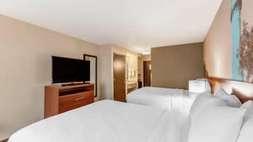 Habitación de hotel con televisor sobre un soporte de madera, cama con ropa blanca, lámpara de noche y puerta que da a un baño.