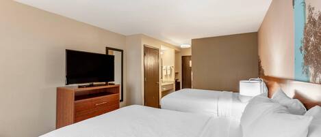 A hotel room with a television on a wooden stand, a bed with white linens, a bedside lamp, and a door leading to a bathroom.