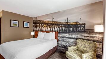Een hotelkamer met een bed, een stoel, een wanddecoratie van een pier en twee ingelijste foto's.