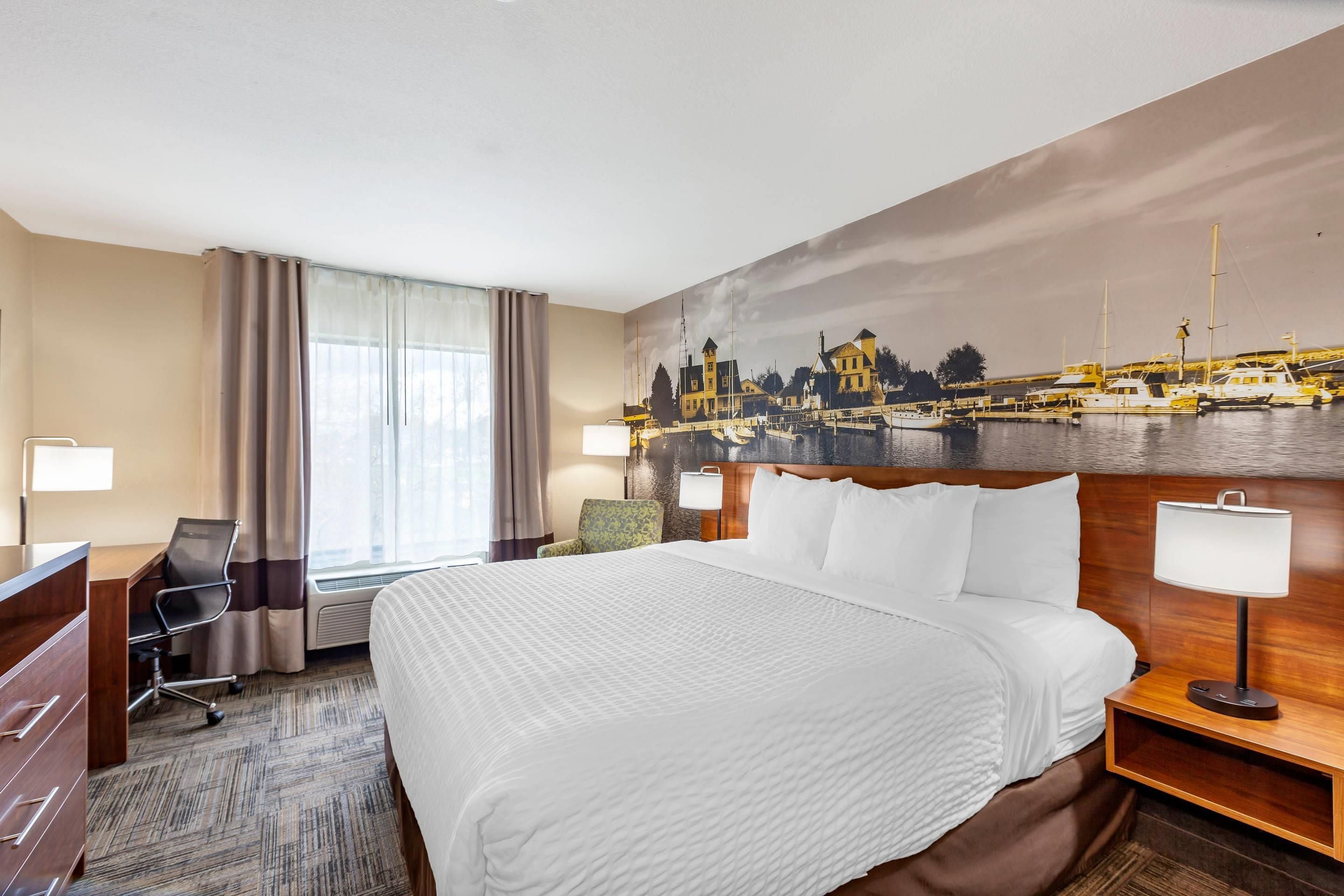 Habitación de hotel con una cama grande, un escritorio, una silla, una mesita de noche y un cuadro de una escena portuaria.