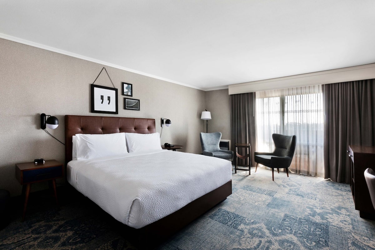 Une chambre d’hôtel avec un grand lit, un bureau, une chaise et une fenêtre avec des rideaux.