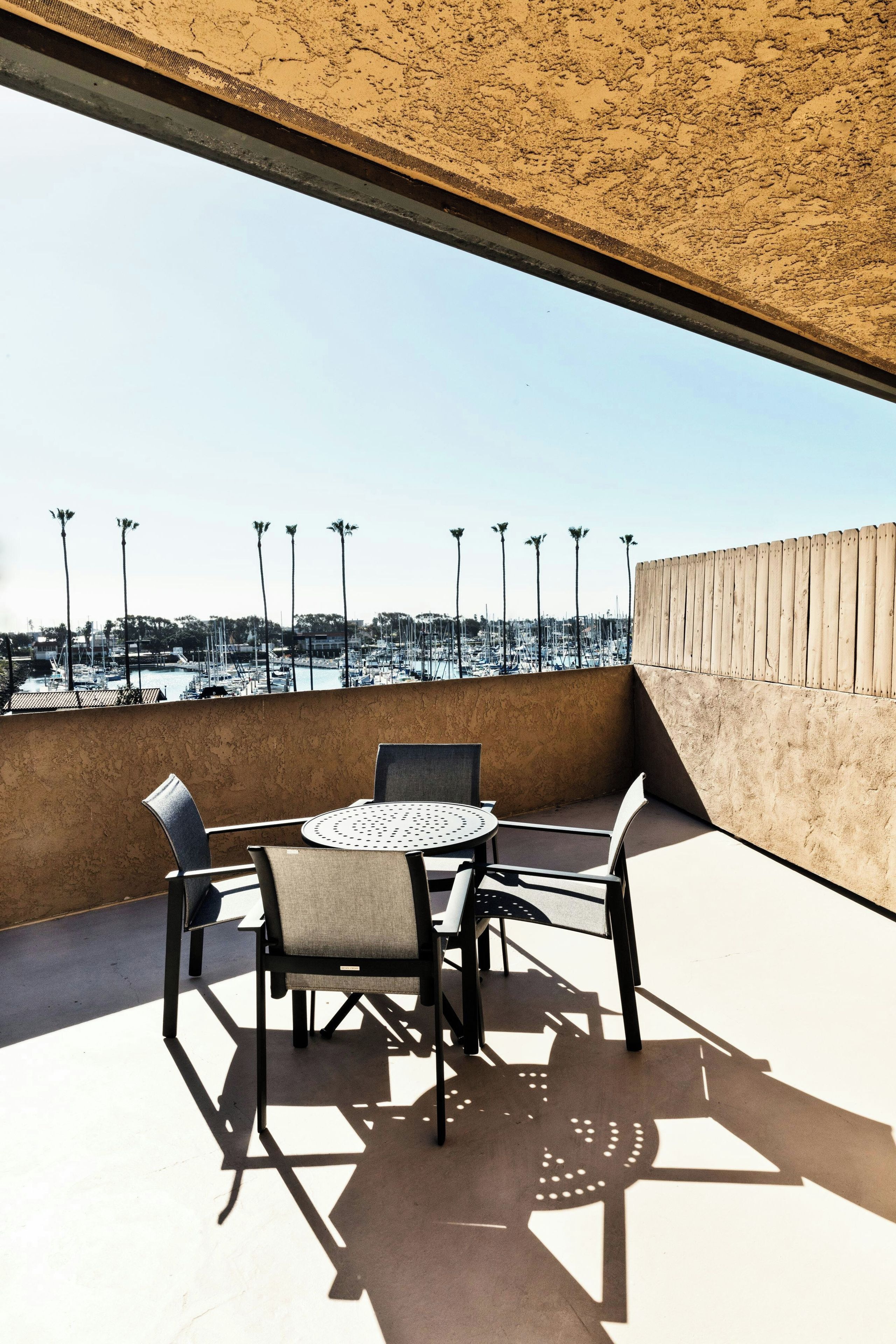 A rooftop terrace with a table and chairs, overlooking a marina with boats and palm trees.