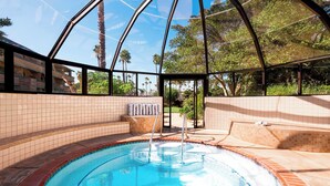 A pool area with a glass enclosure, tiled walls, and a view of palm trees and buildings.