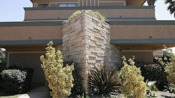 Un edificio a più piani con una torre centrale in pietra, un tetto piatto e un giardino anteriore curato con arbusti e piante varie.