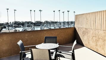 A rooftop terrace with a round table and chairs, overlooking a marina with boats and palm trees.