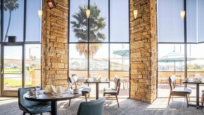 An indoor dining area with brick walls, large windows, and a view of the outdoors. Tables are set with chairs and dining ware.