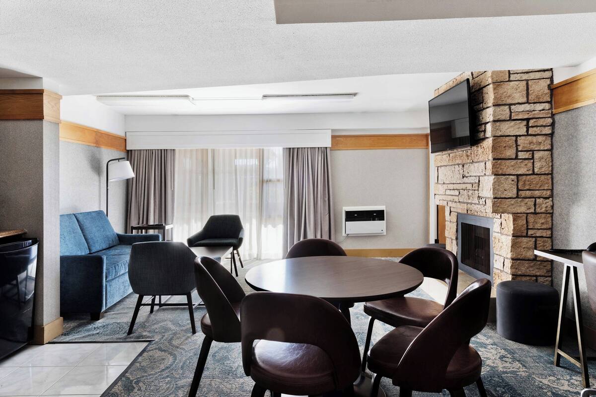 Une chambre d’hôtel moderne dotée d’un coin repas, d’un canapé, d’une cheminée et d’un téléviseur fixé au mur.