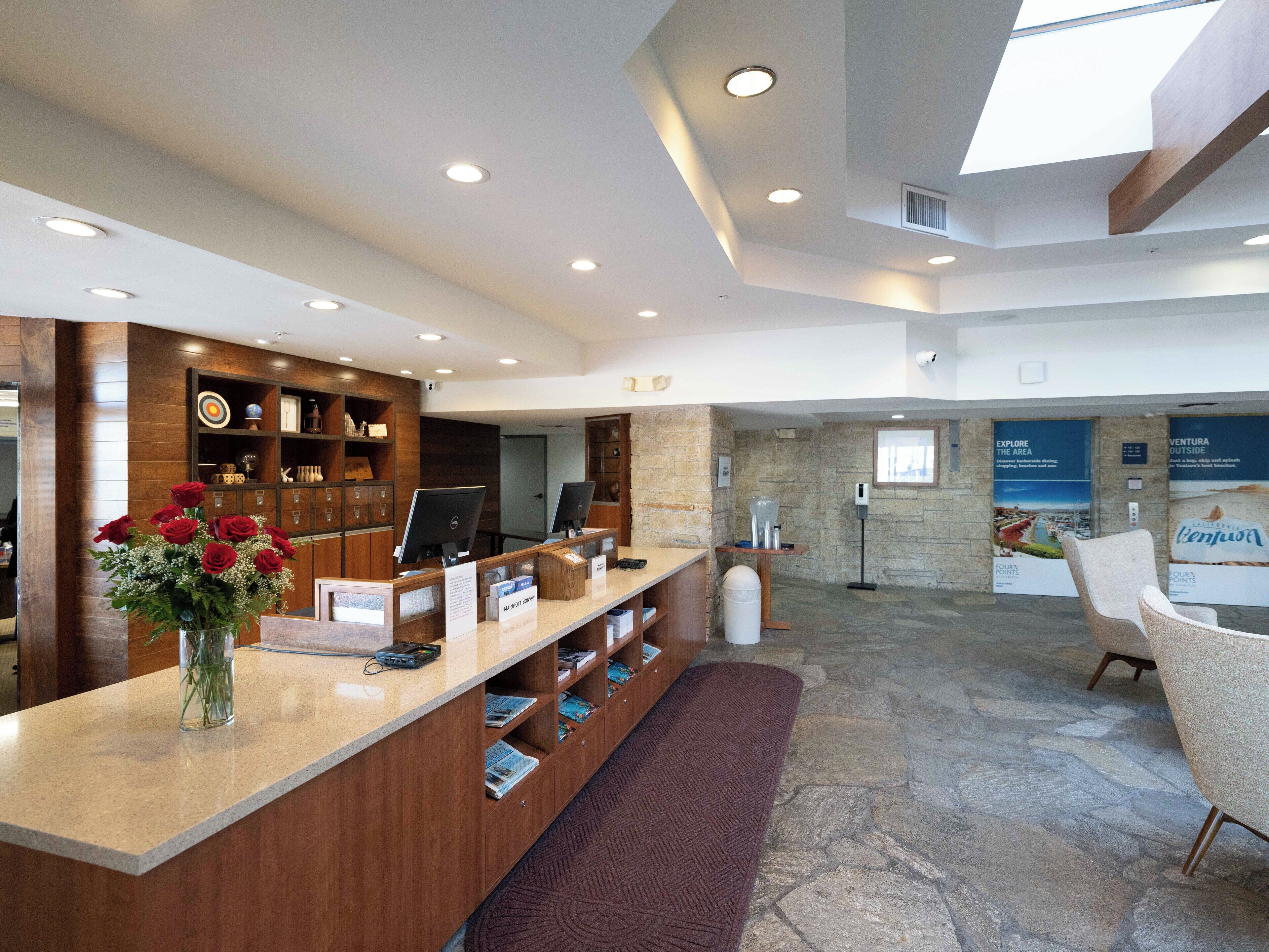 A reception area with a wooden reception desk, a vase of red roses, a stone wall, and a seating area with a chair.