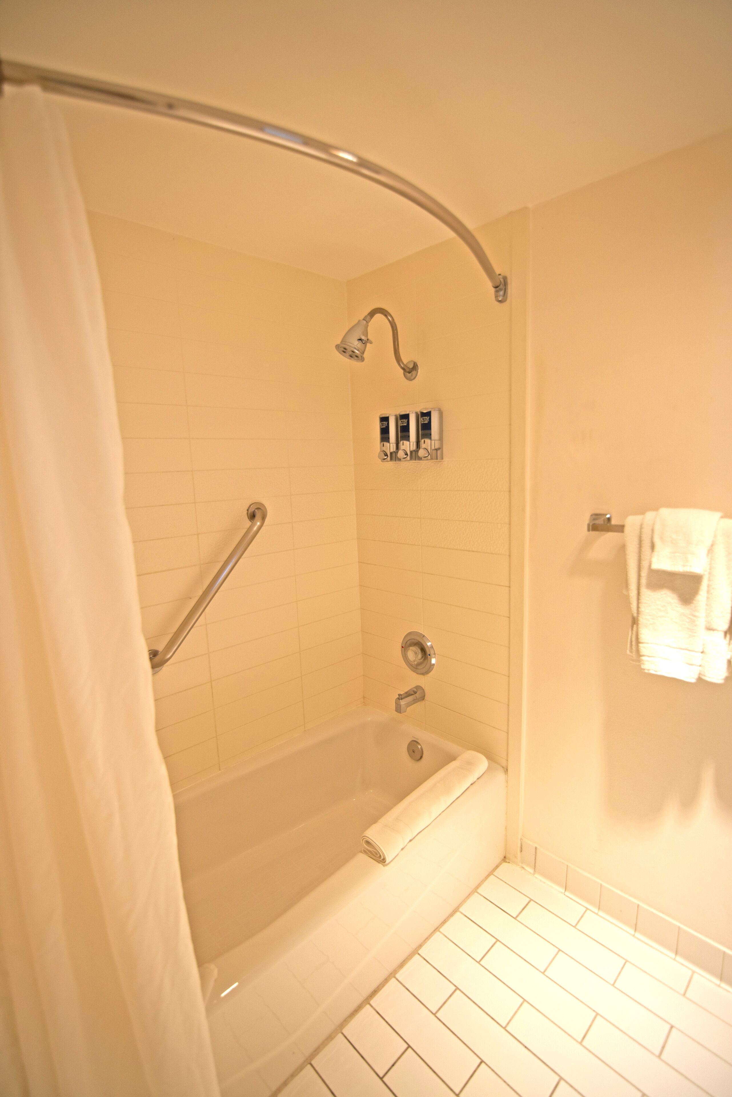 Un baño con bañera, cortina de ducha, barra de apoyo y toallero.