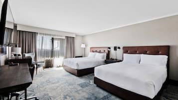 Ein Hotelzimmer mit zwei Betten, einem Schreibtisch, einem Stuhl, einer Lampe und einem großen Fenster mit Vorhängen.