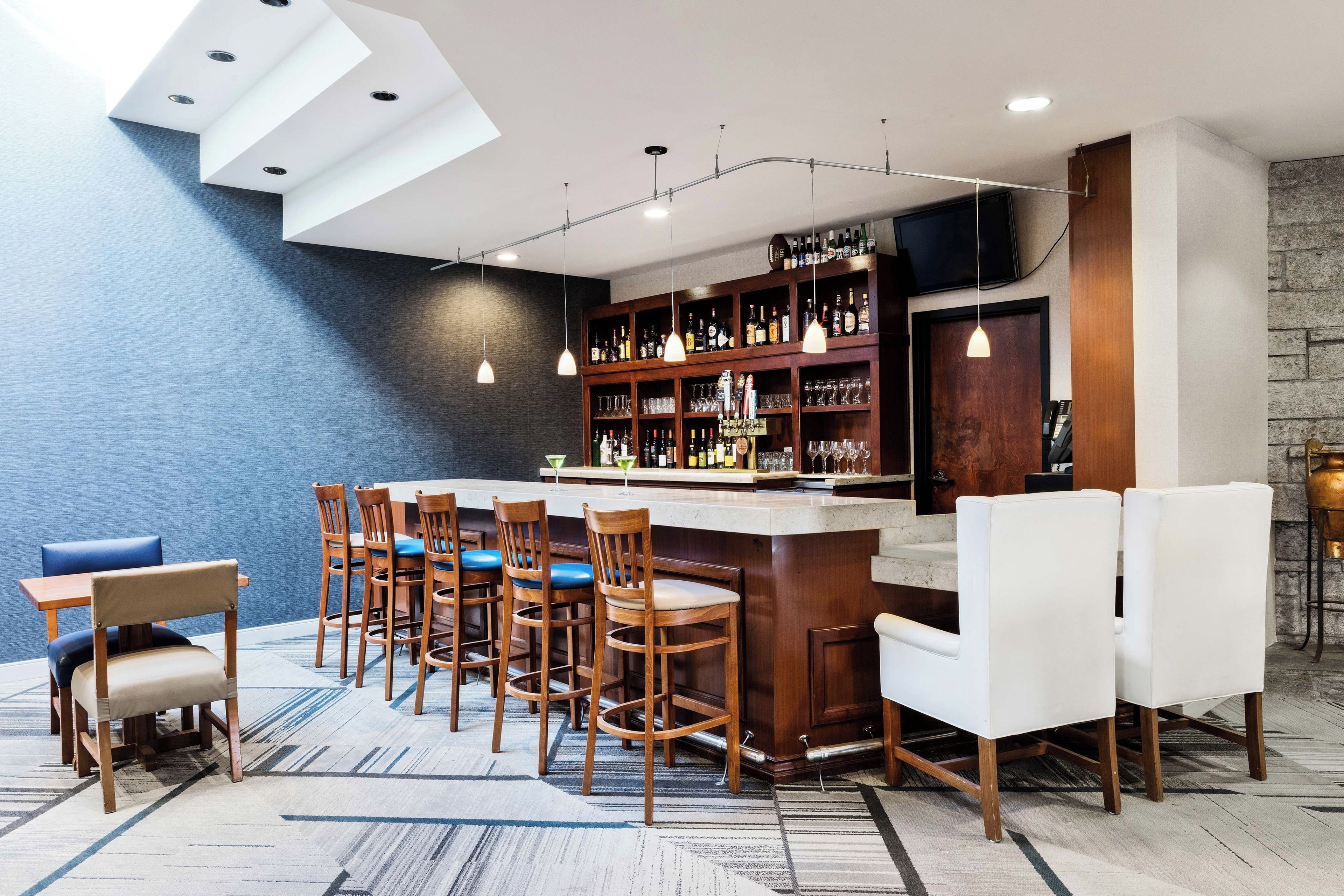 A bar area with a counter, bar stools, and a selection of bottles and glasses.