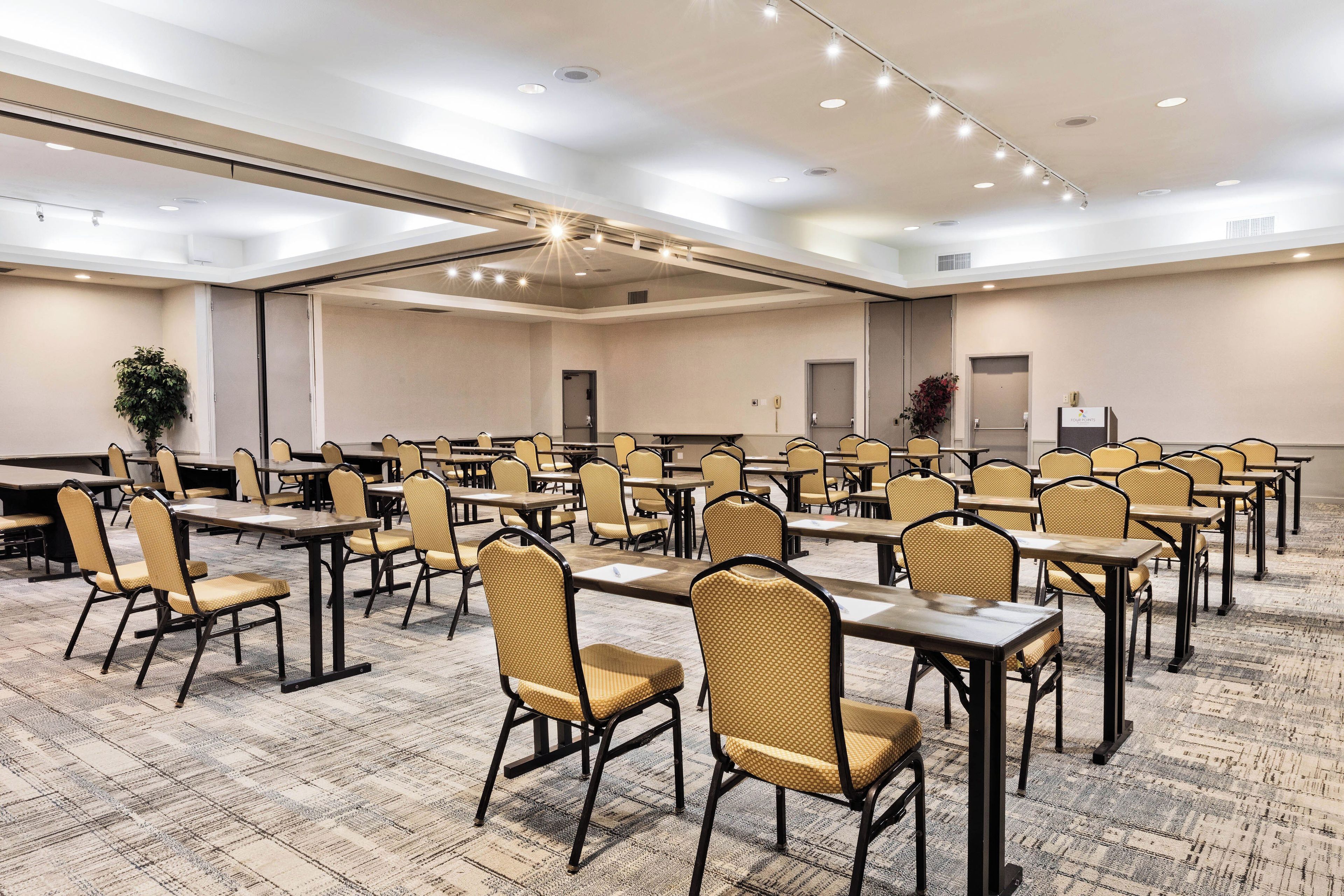 A large conference room with multiple tables and chairs, carpeted flooring, and recessed ceiling lighting.