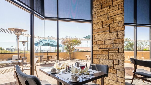An outdoor dining area with tables set for two, large windows, and a view of the surrounding landscape.