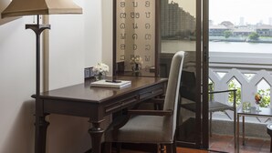 A room with a desk, chair, lamp, and a view of a cityscape through a window.