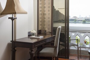 A room with a desk, chair, lamp, and a view of a cityscape through a window.