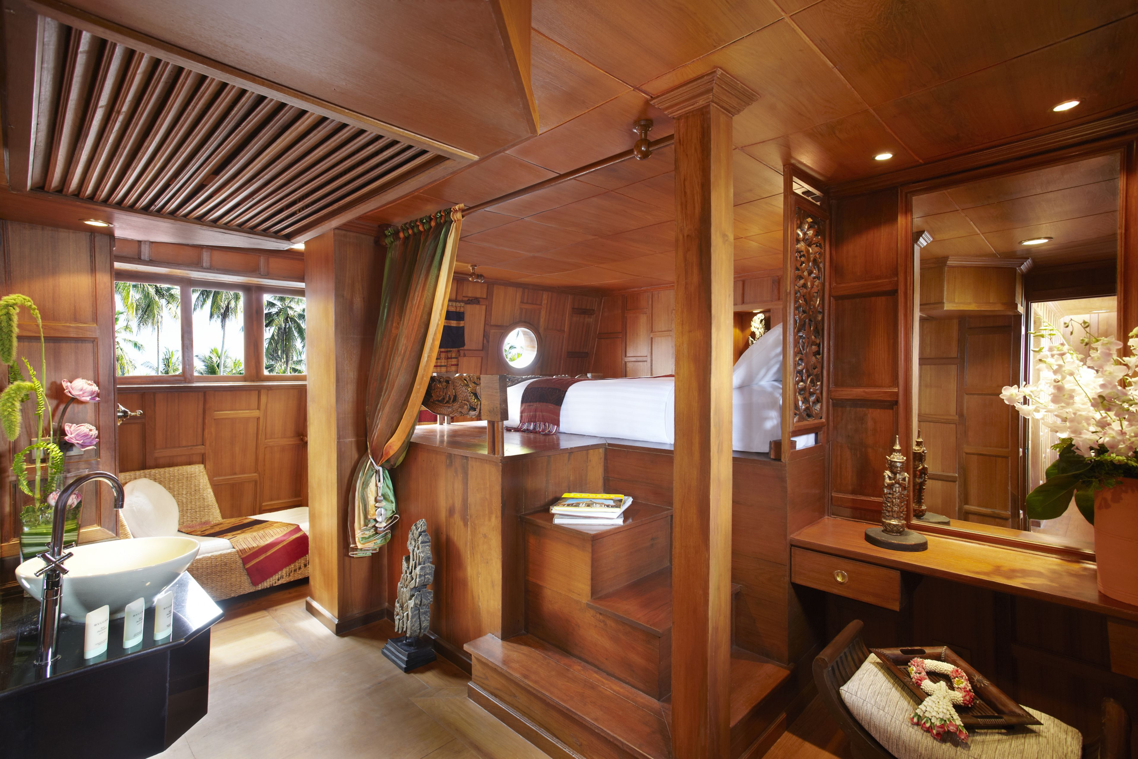 Een houten interieur met een groot raam, een wastafel, een bed en een spiegel.