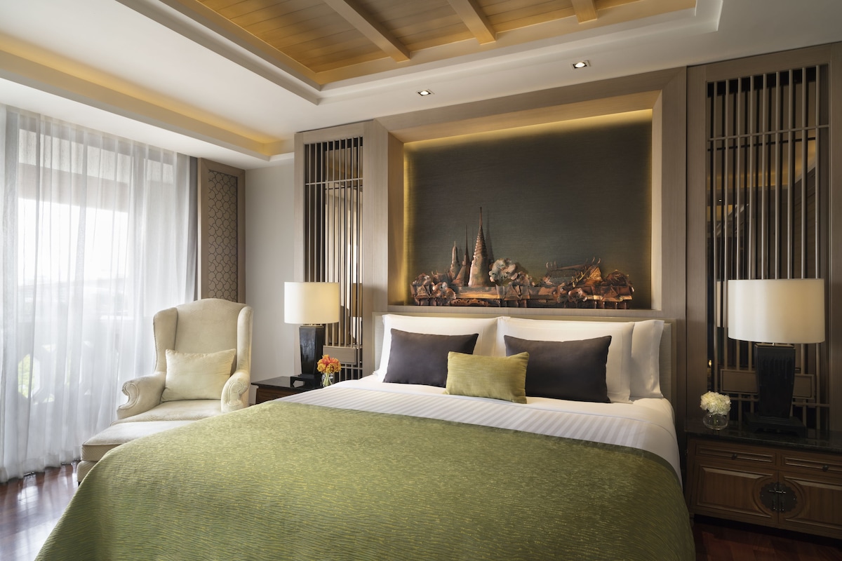 A hotel room with a large bed, two bedside tables, a chair, and a decorative wall piece.