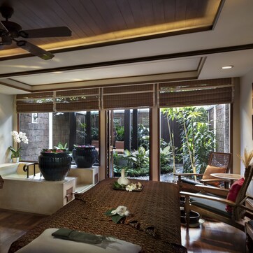 A spa room with a massage table, a bathtub, and a seating area with a view of the garden.