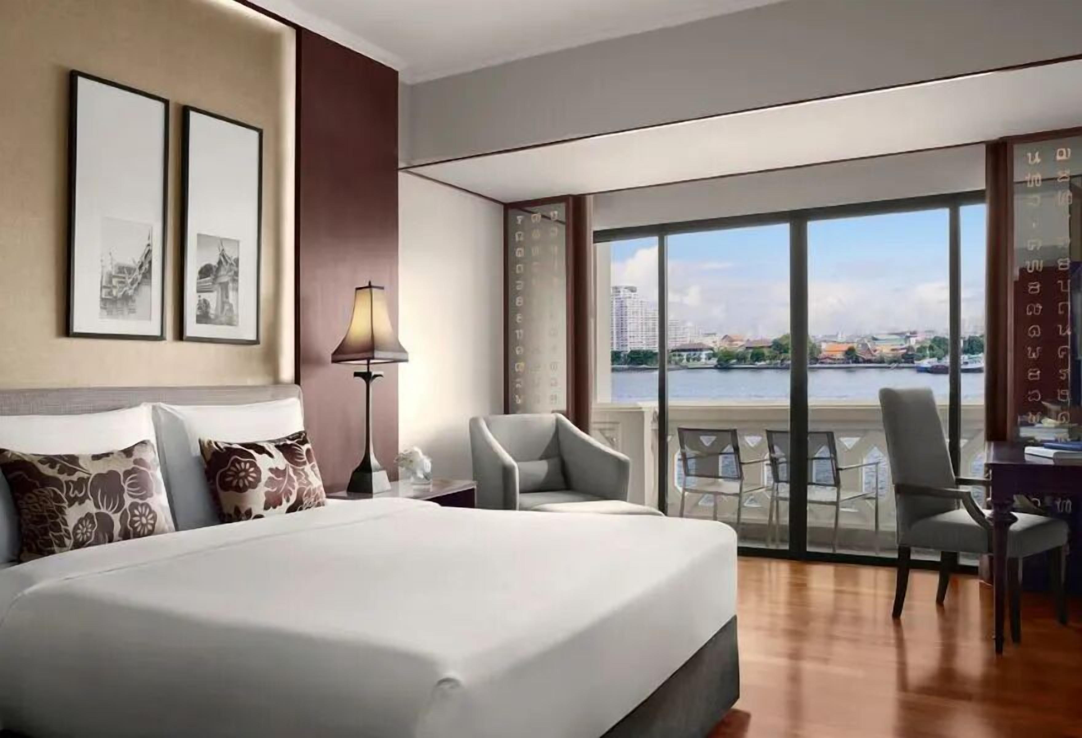 A hotel room with a large bed, two chairs, a desk, and a view of a body of water.