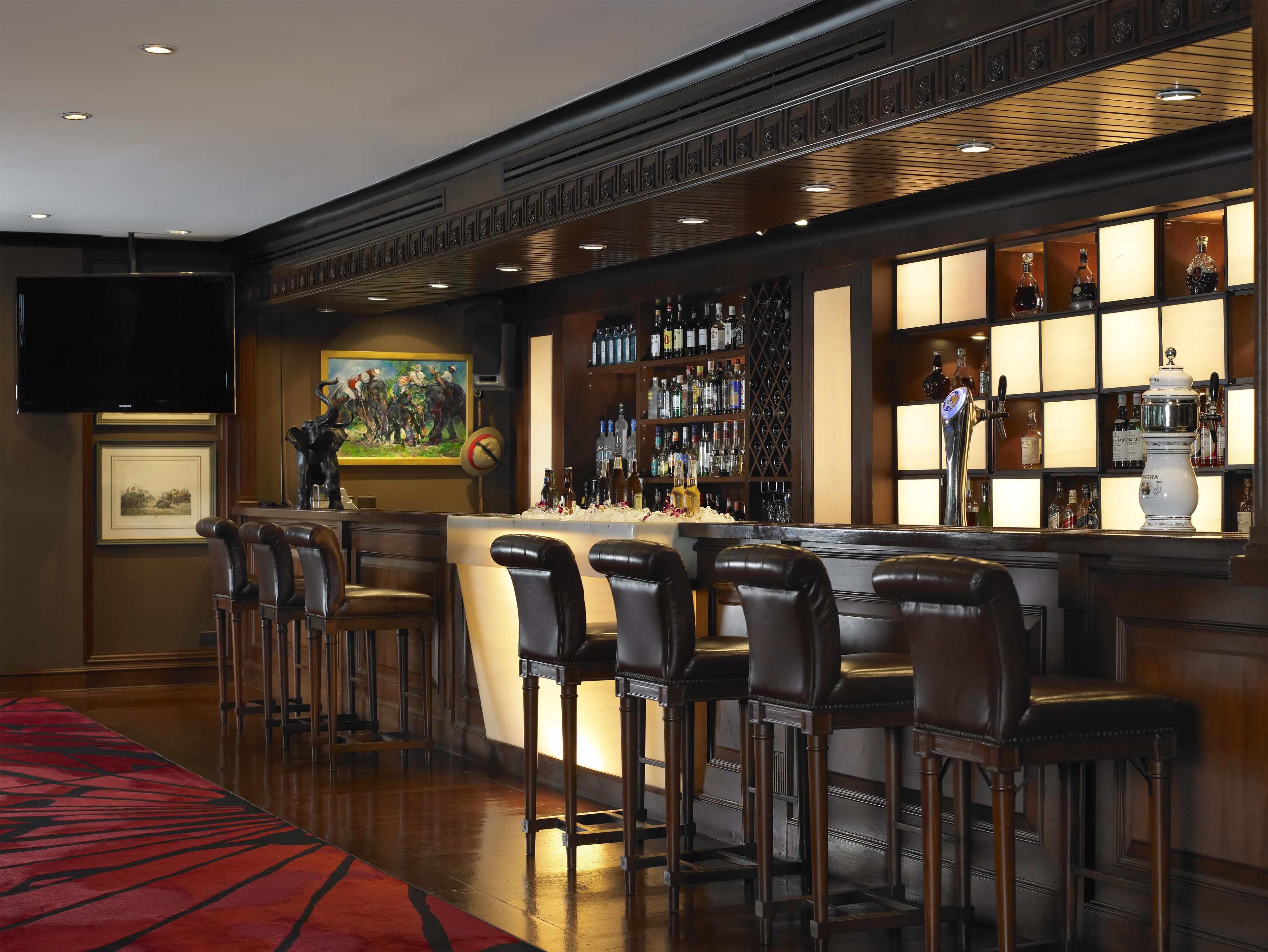 A bar area with a long counter, multiple stools, and a variety of bottles and glasses.