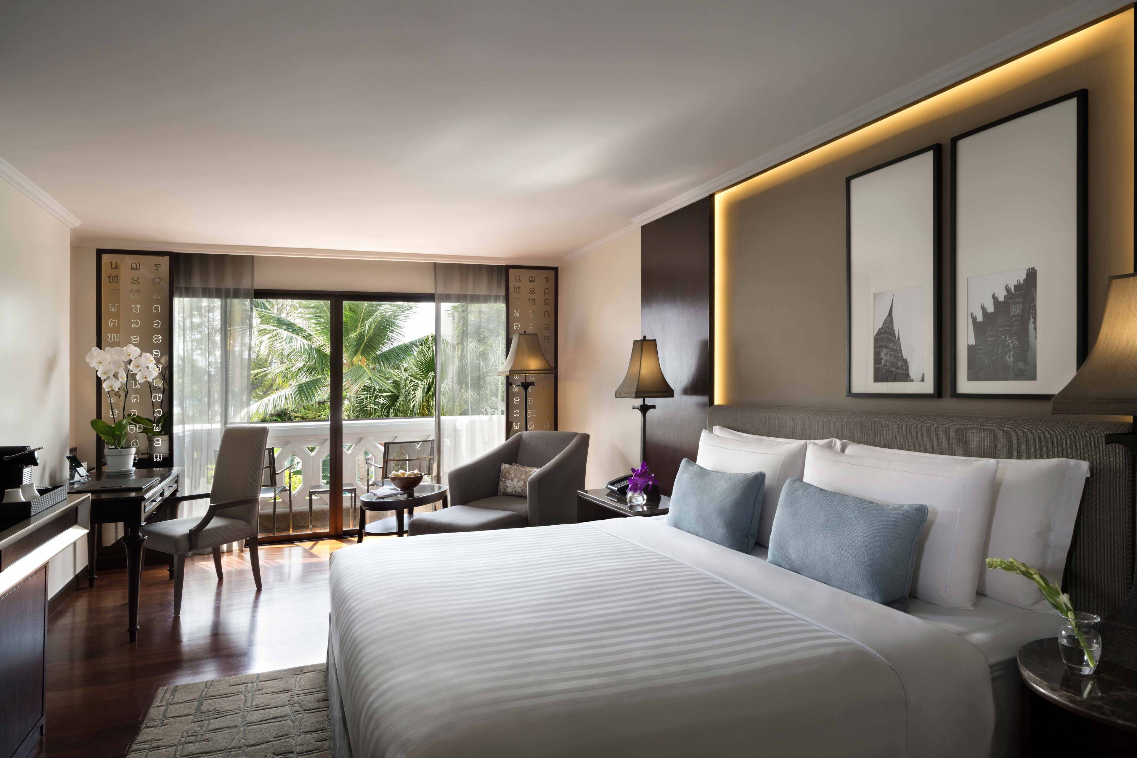 A hotel room with a large bed, two chairs, a desk, a lamp, and framed pictures on the wall.