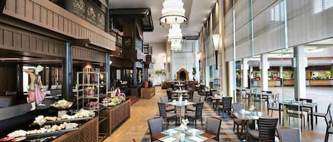 Un amplio vestíbulo de hotel con una zona de estar central, un bufé con diferentes opciones de comida y vistas al exterior a través de amplias ventanas.