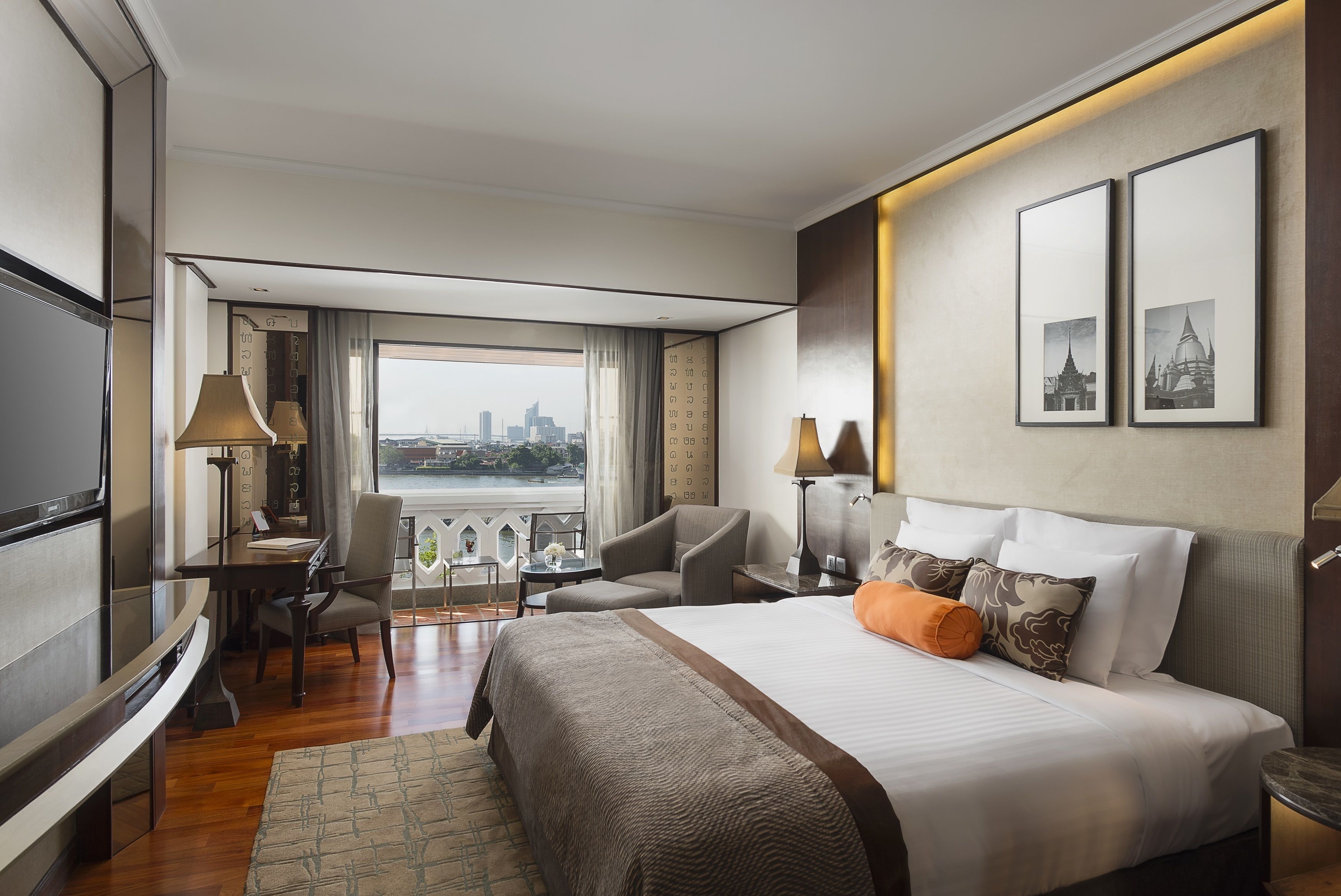 Habitación de hotel con una cama grande, un escritorio, una silla y un televisor. Se ve una vista panorámica de la ciudad a través de la ventana.