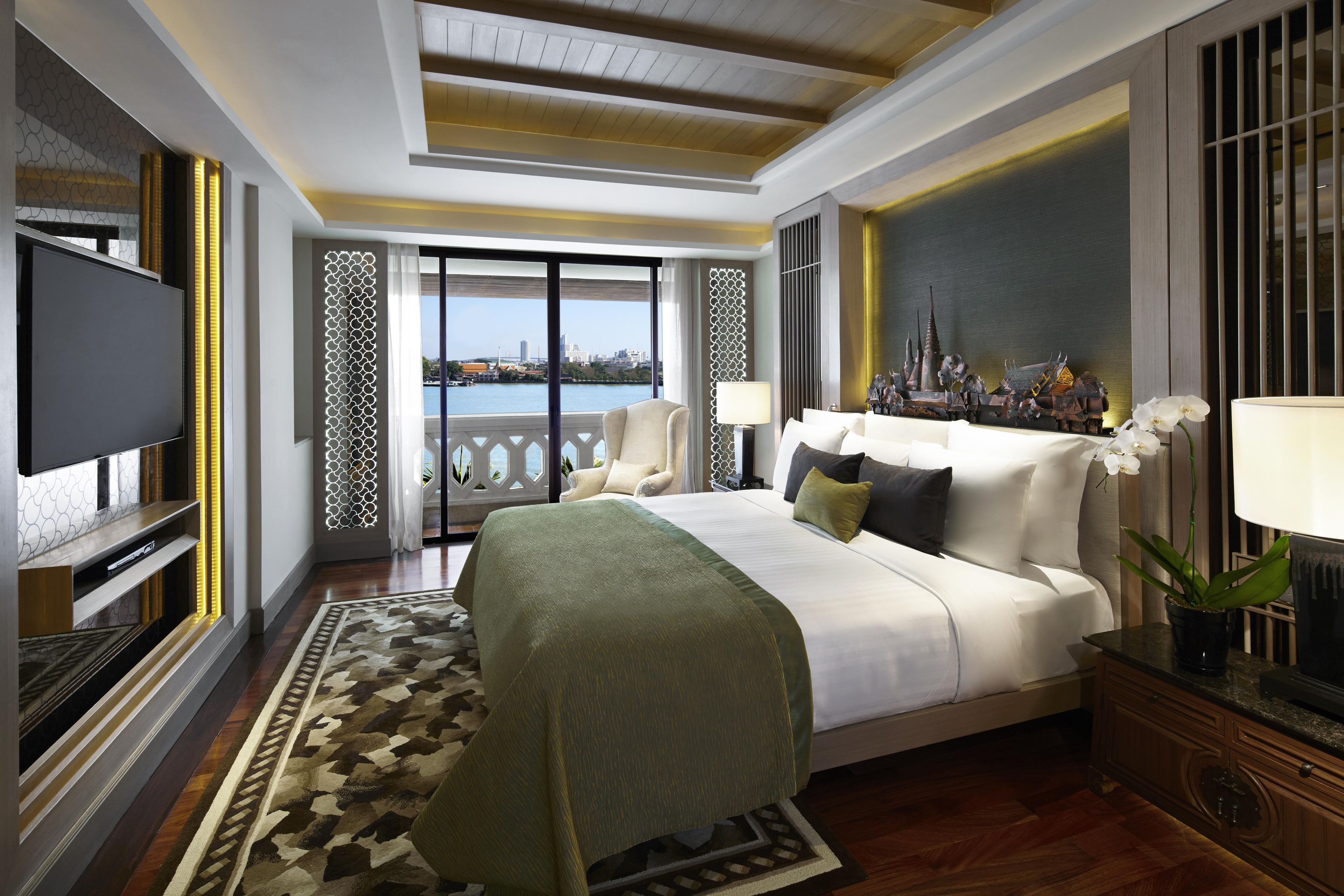 Una habitación de hotel moderna con una cama grande, un televisor, un balcón con vistas a la ciudad y detalles decorativos.
