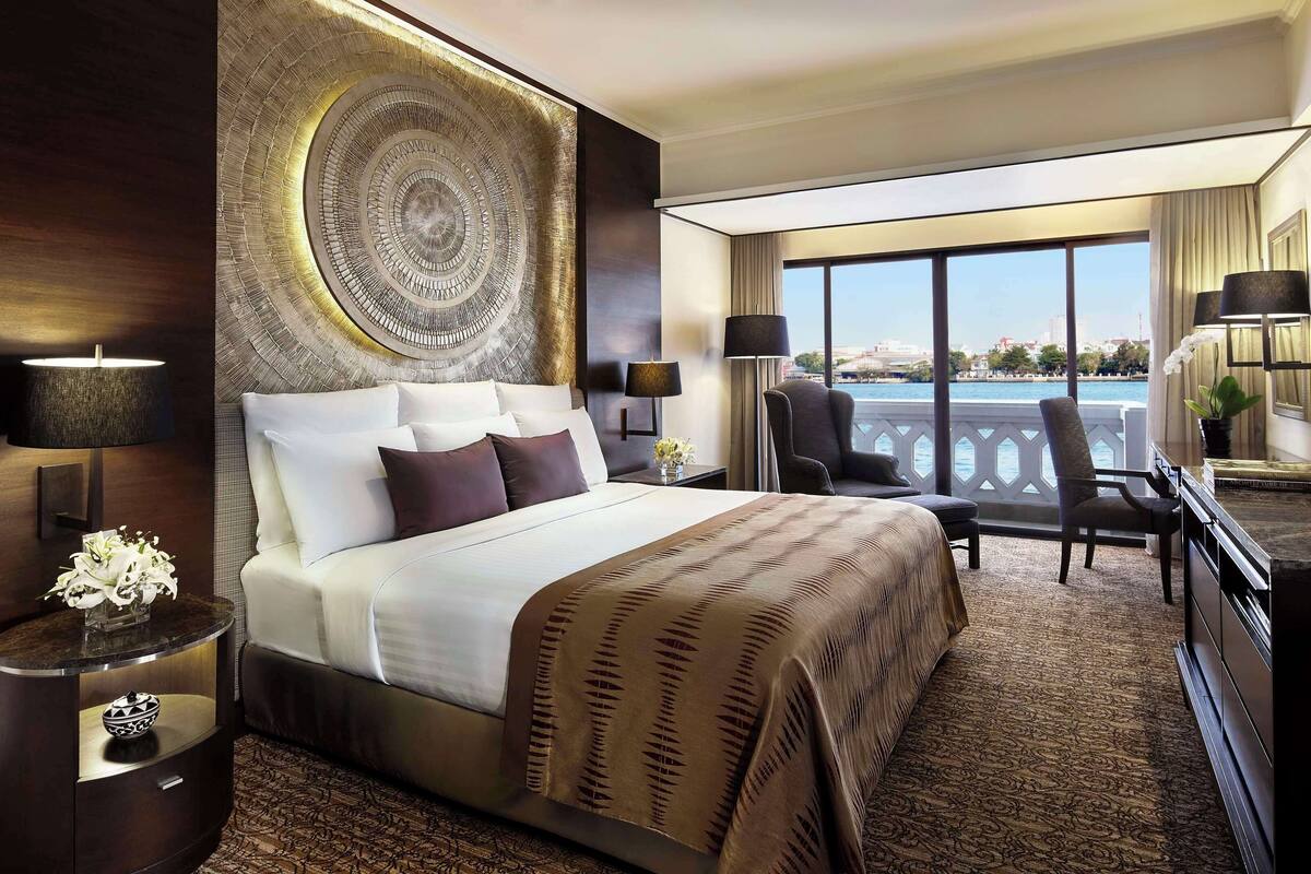 A hotel room with a large bed, a desk, a chair, a TV, and a view of the water.