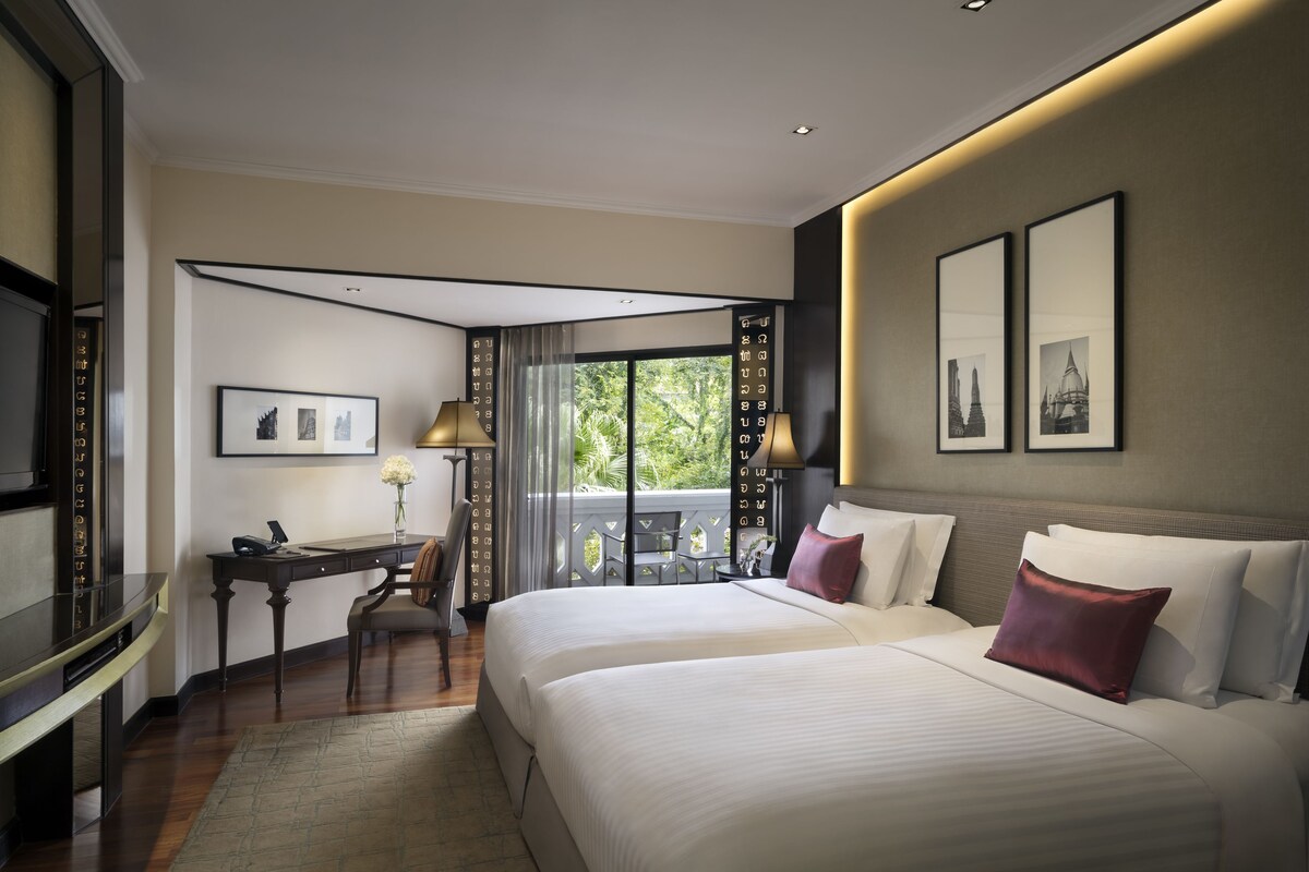 A hotel room with two beds, a desk, and a balcony with a view.