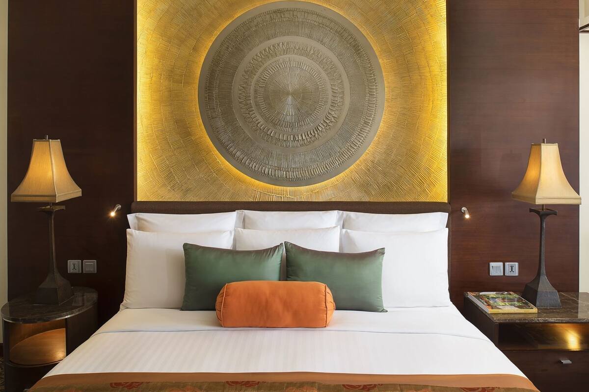 A hotel room with a large bed, two bedside lamps, and a decorative wall piece.
