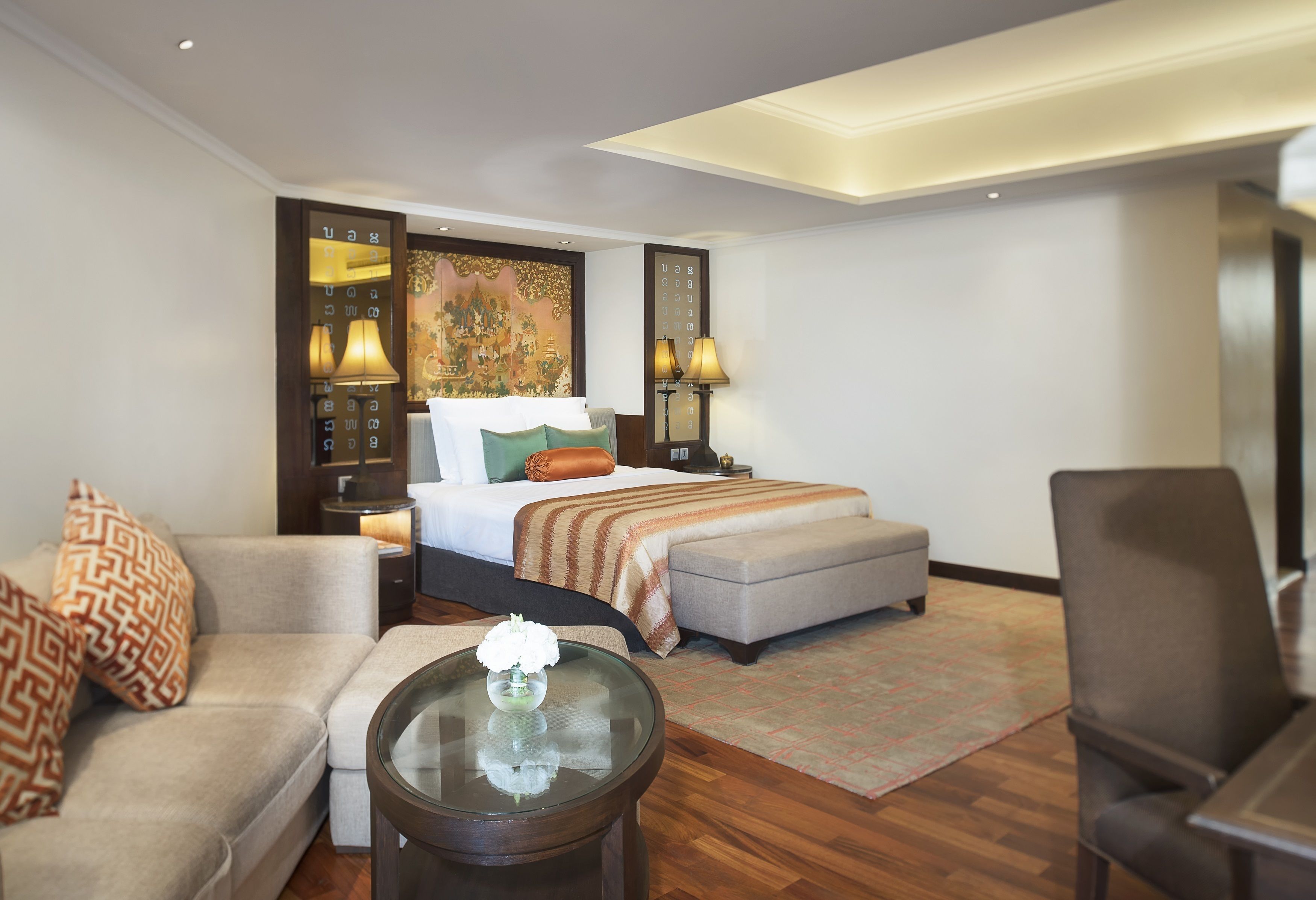 Una habitación de hotel con una cama, un sofá, una silla, una mesita pequeña y una mesita de noche con lámparas.