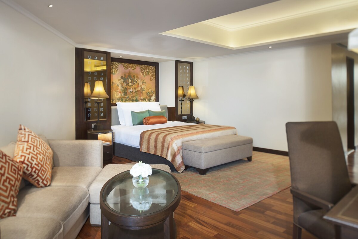 A hotel room with a bed, a sofa, a chair, a small table, and a nightstand with lamps.