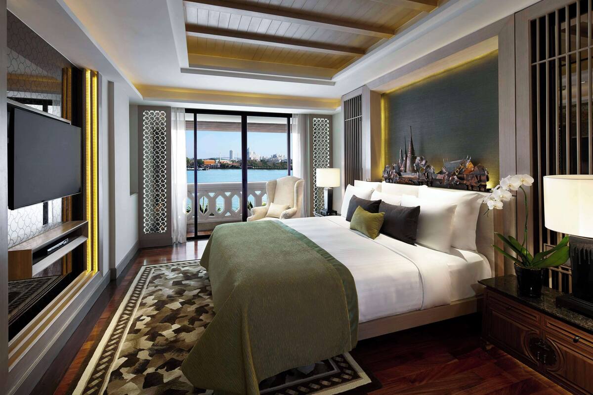 A spacious hotel room with a large bed, a television, a balcony with a view of the city, and a decorative wall.